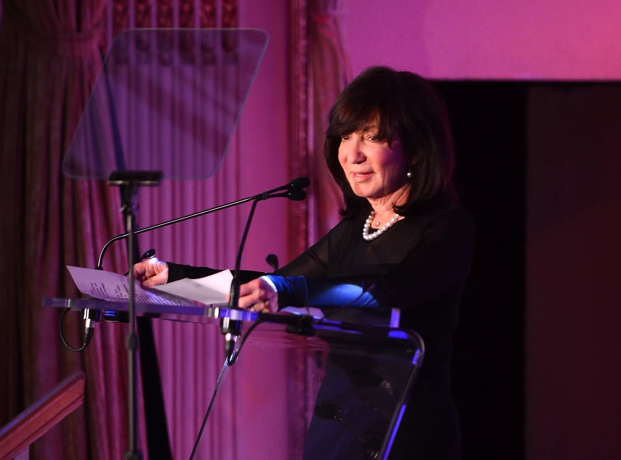 photo of a woman standing at a podium and speaking into a microphone