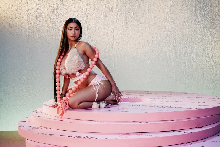 A woman is posing, sitting on a pink rug.
