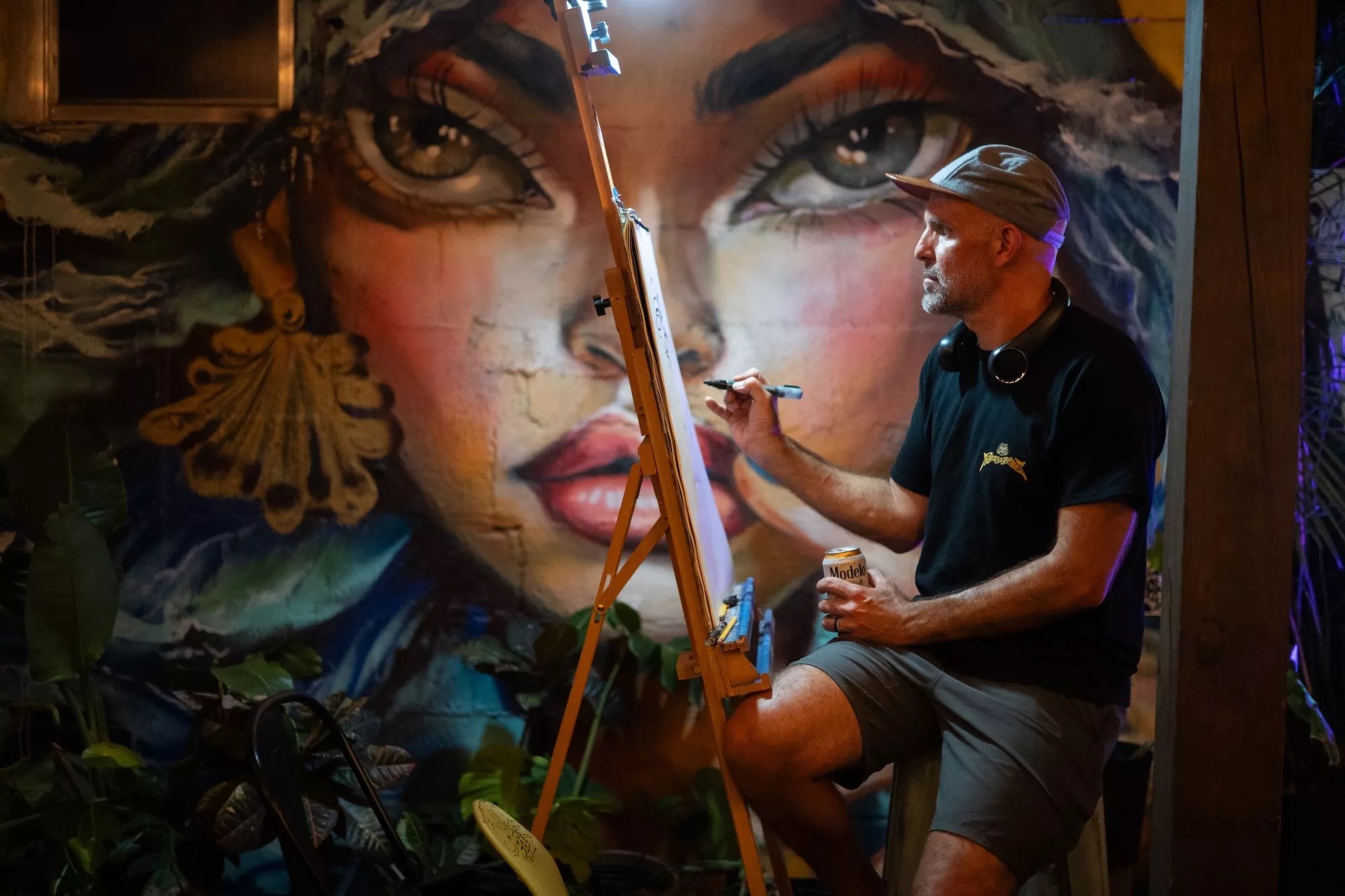 a man paints on a canvas in front of a mural of a woman's face