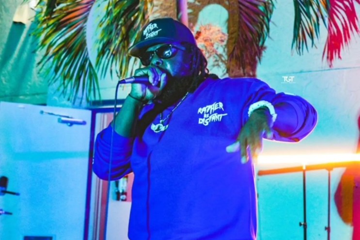 Picture of a man wearing a hat and rapping while holding a microphone.